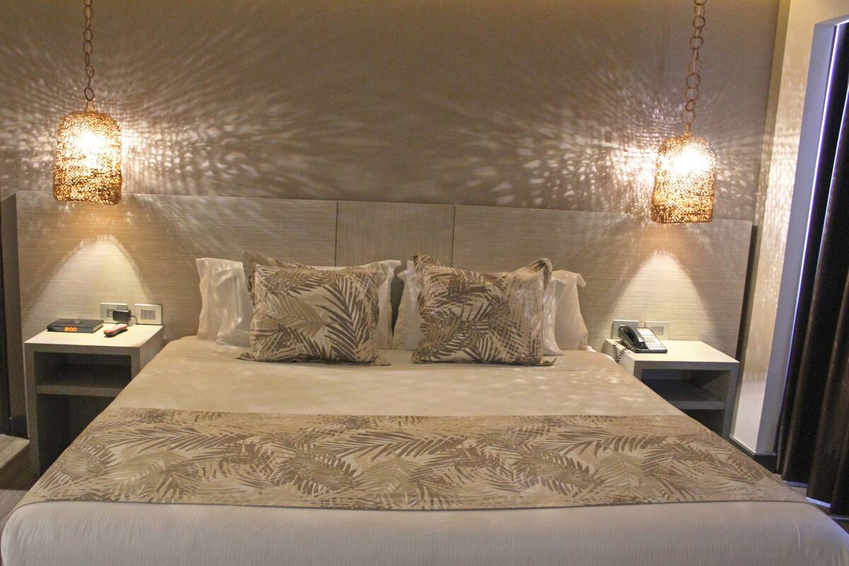 Una habitación de hotel con una cama grande, dos mesitas de noche y dos lámparas de pared.
