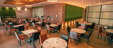 A modern restaurant with round tables and chairs, a wooden ceiling, and a green accent wall.