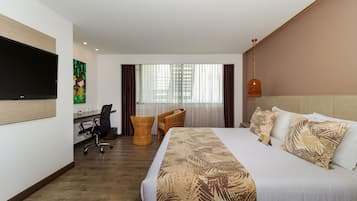 A hotel room with a large bed, a desk, a chair, a TV, and a window with curtains.