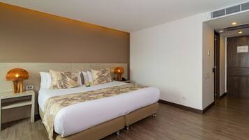 A modern hotel room with a large bed, wooden flooring, and a nightstand with a lamp.