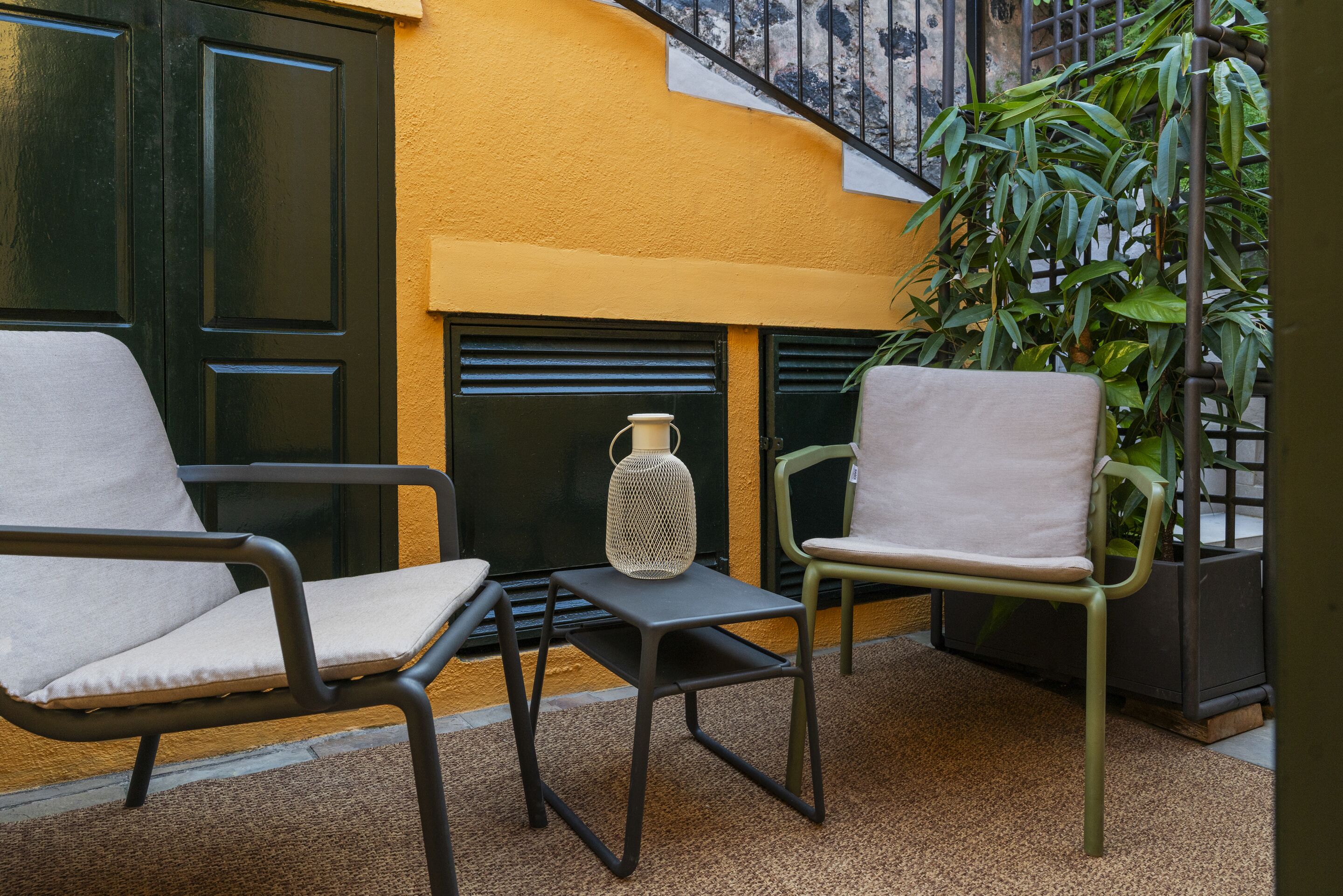 Un área de estar al aire libre acogedora, con dos sillas y una mesita, un jarrón decorativo y una planta en maceta.