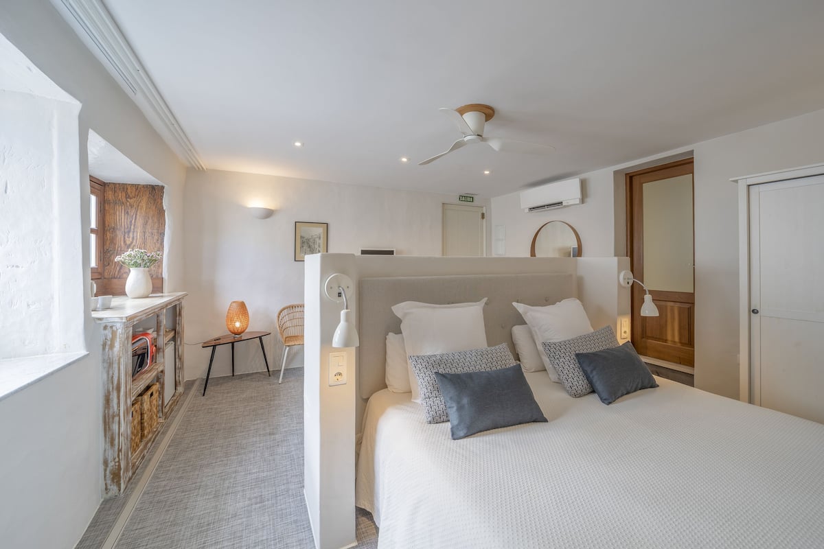 Een slaapkamer met een bed, nachtkastje, lamp en een plafondventilator.