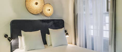 Una cama bien hecha con ropa de cama blanca y negra, un cabecero oscuro y dos lámparas fijadas a la pared.