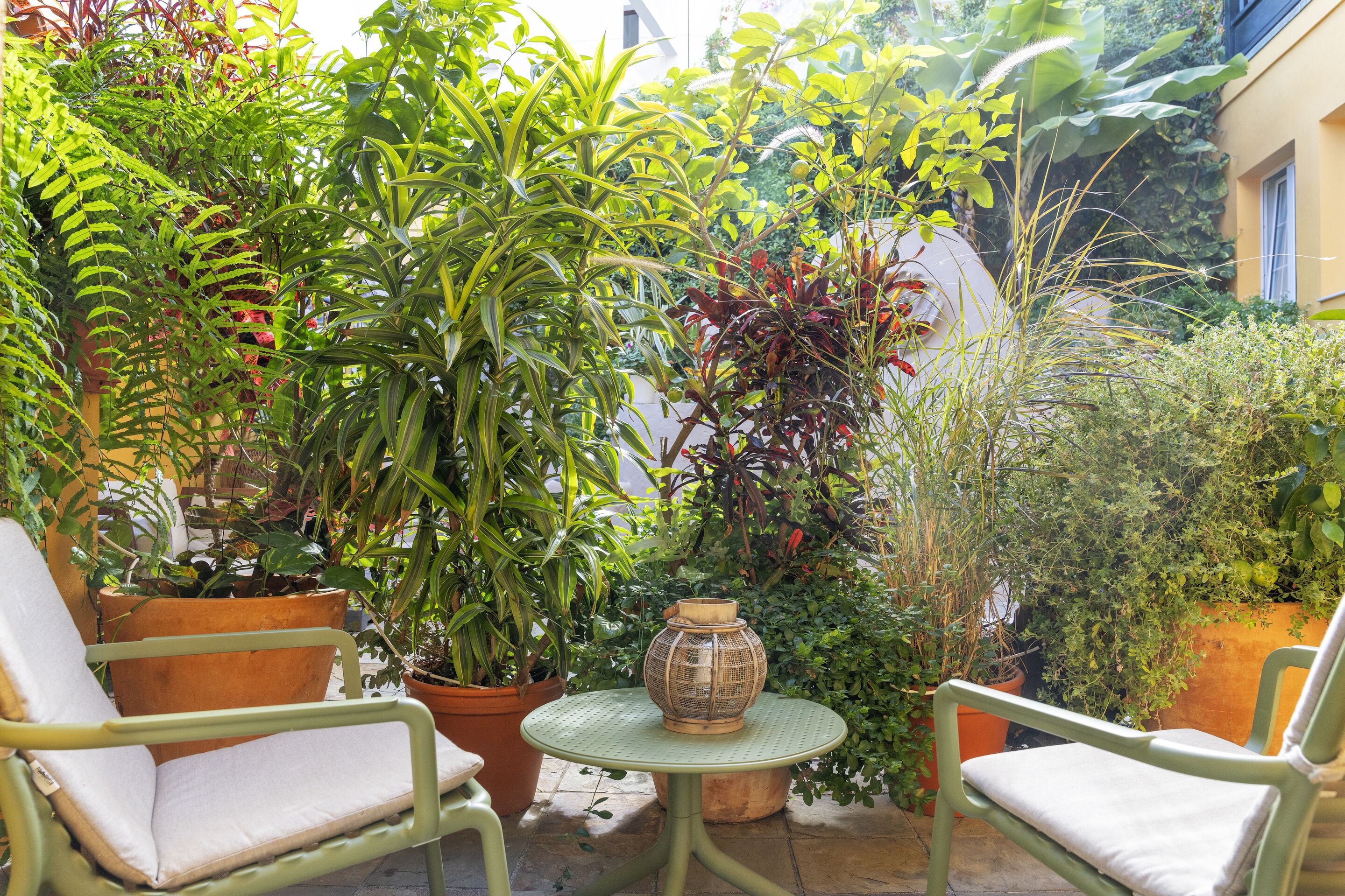 A small patio area with two green chairs, a round table, and various potted plants.