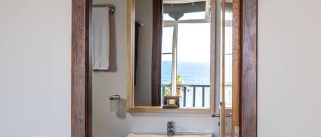 A bathroom with a white sink, a wooden-framed mirror, and a view of the sea through a window.