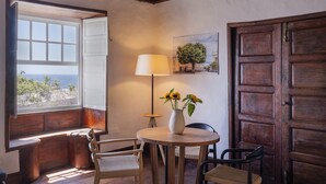Een gezellige kamer met een houten bankje, een ronde tafel met een bloevas, en uitzicht op de zee door een open raam.