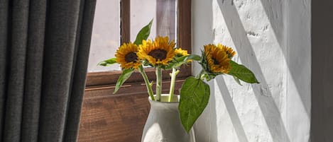 Et vindue med en hvid vase med solsikker på et hvidt vindueskar.