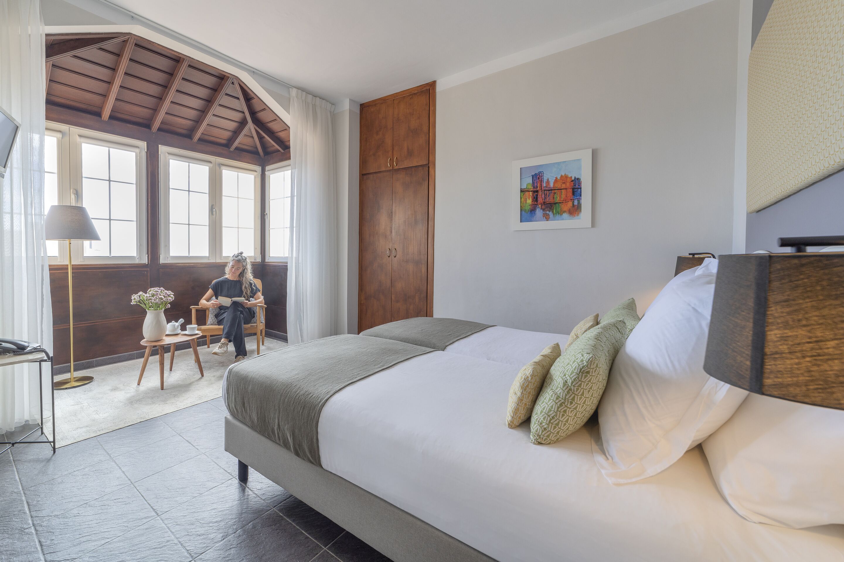 A bedroom with a large bed, a wooden wardrobe, a window with curtains, and a painting on the wall.