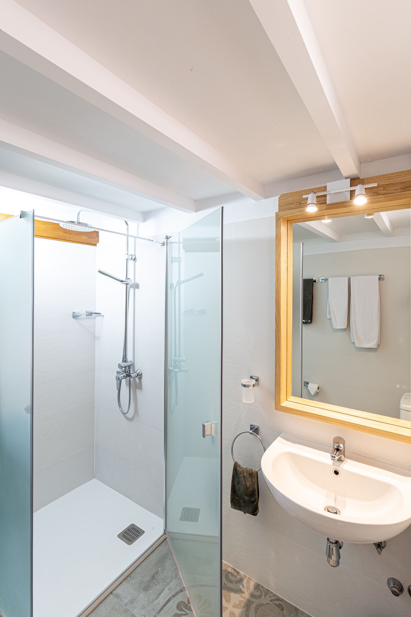 A modern bathroom with a glass-enclosed shower, a white sink, and a mirror with a wooden frame.