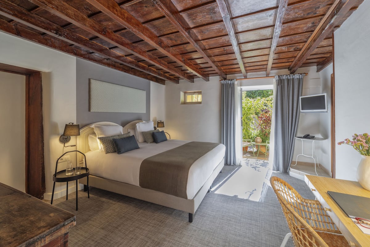 Een slaapkamer met een groot bed, een bureau met stoel, een televisie en uitzicht op de omgeving.