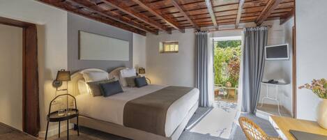 A bedroom with a large bed, a desk with a chair, a TV, and a view of the outdoors.