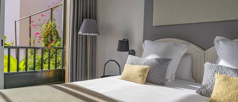 A hotel room with a bed, a nightstand, a lamp, and a view of a balcony with greenery.