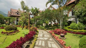 A garden pathway leading to a building with a tiled roof, surrounded by lush greenery and flowering plants. - Royal Hotel and Villa Batu (Batu)