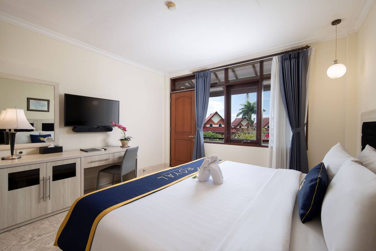 Une chambre d’hôtel équipée d’un lit, d’un bureau, d’une chaise, d’une télévision et d’une fenêtre avec des rideaux.