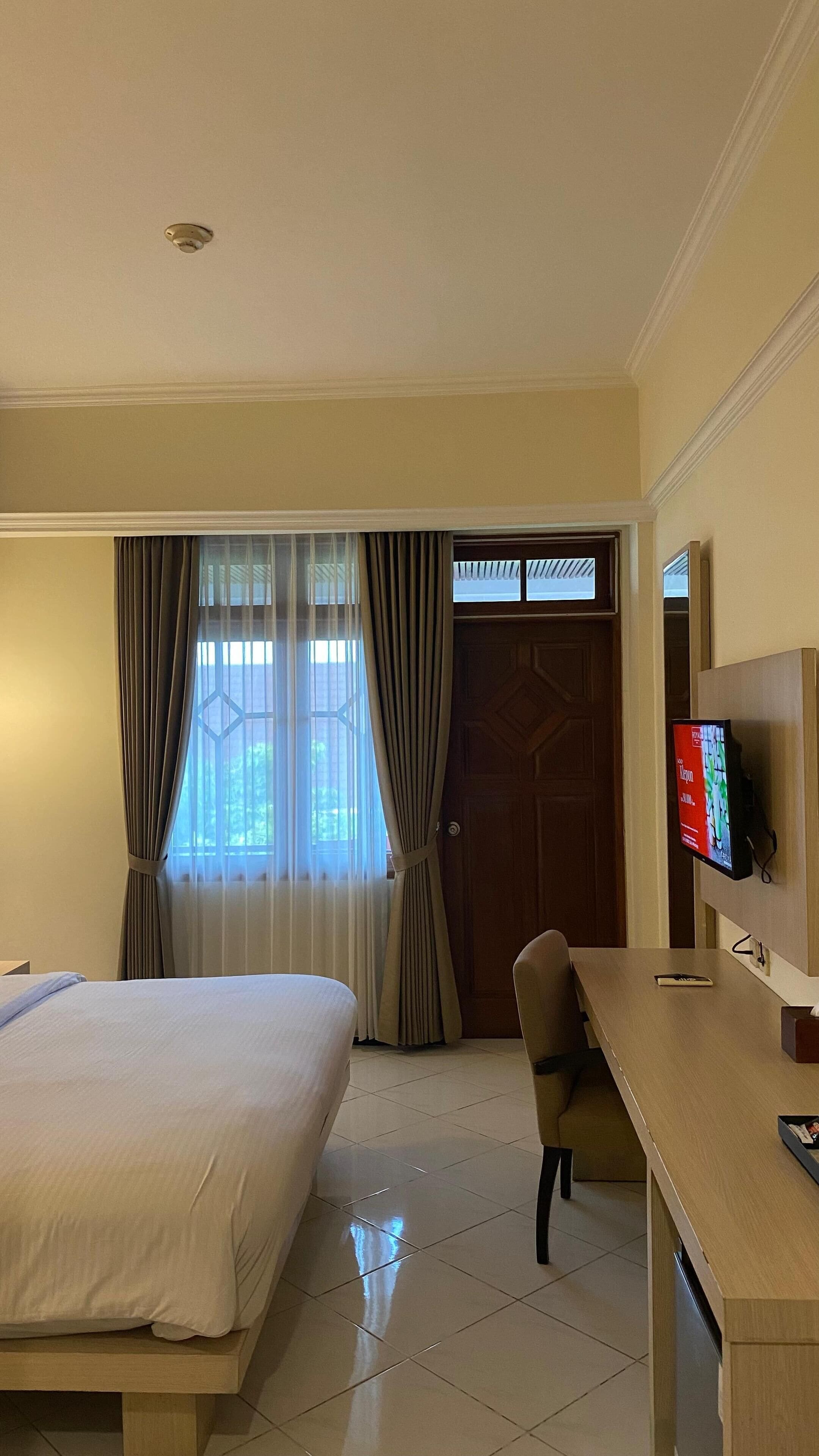 A hotel room with a bed, a desk, a television, and a door.
