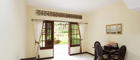 A room with a dining table, chairs, a telephone, and a view of a garden through open doors.