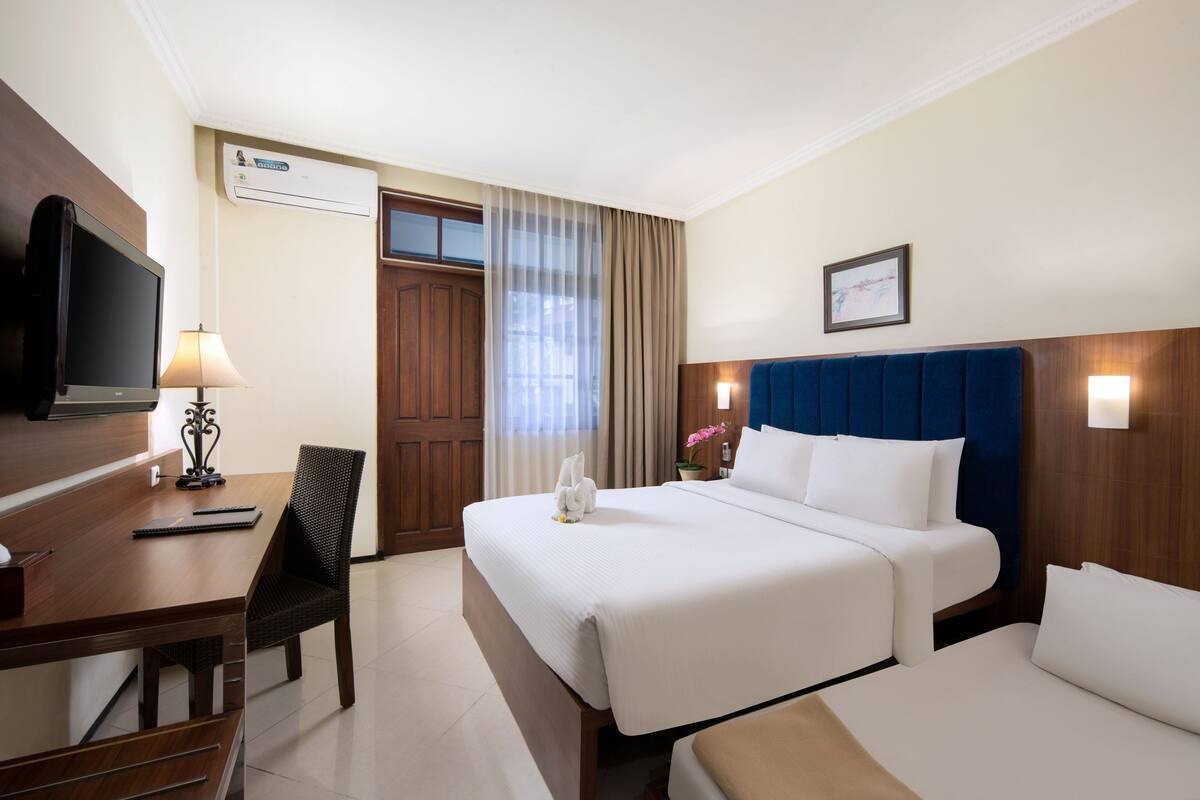 Une chambre d’hôtel équipée d’un lit, d’un bureau, d’une chaise, d’une télévision et d’une fenêtre avec des rideaux.