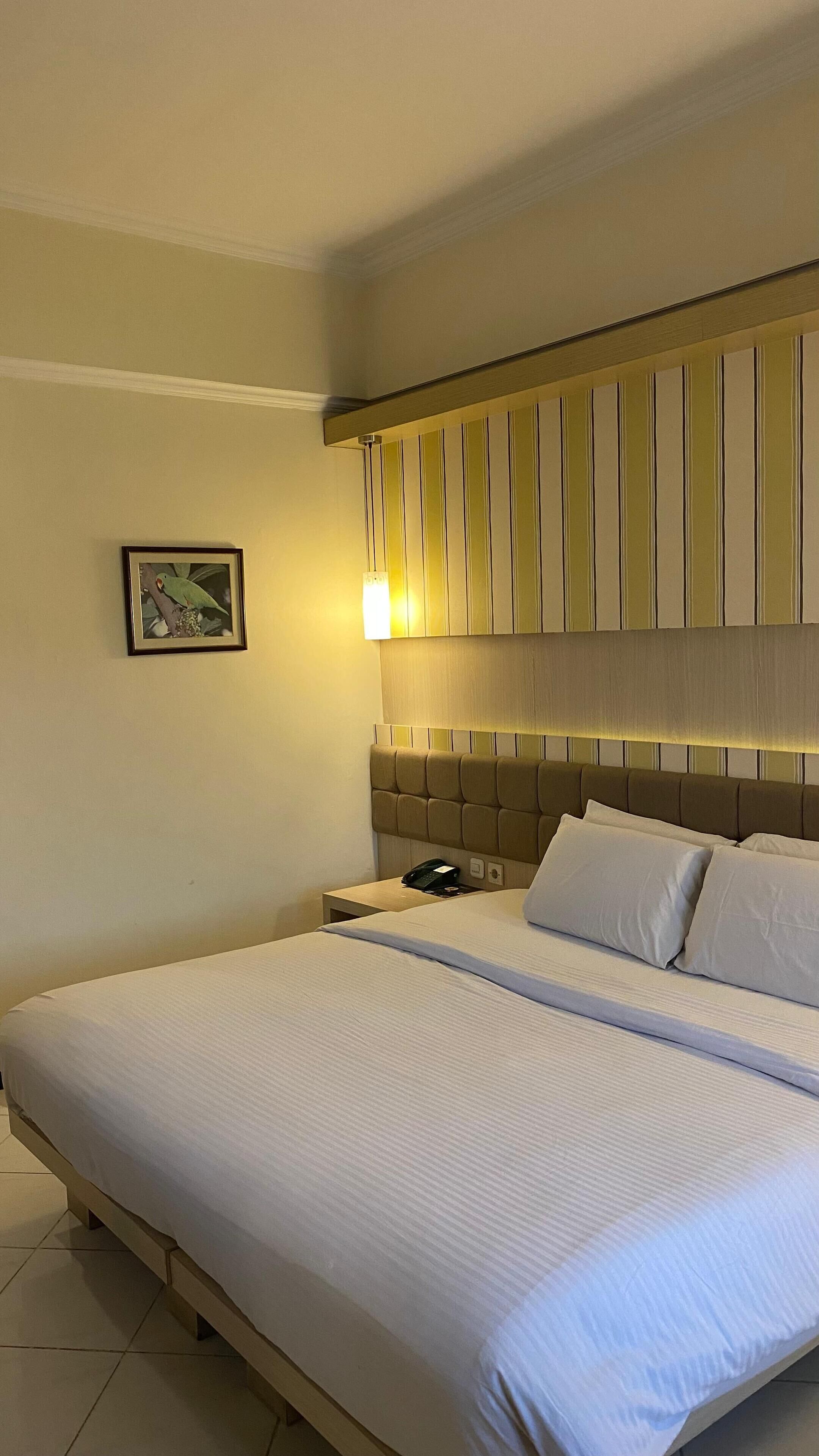Ein Hotelzimmer mit einem großen Bett, einem Kopfteil mit vertikalen Streifen, einem Nachttischchen mit Telefon und einem gerahmten Bild an der Wand.