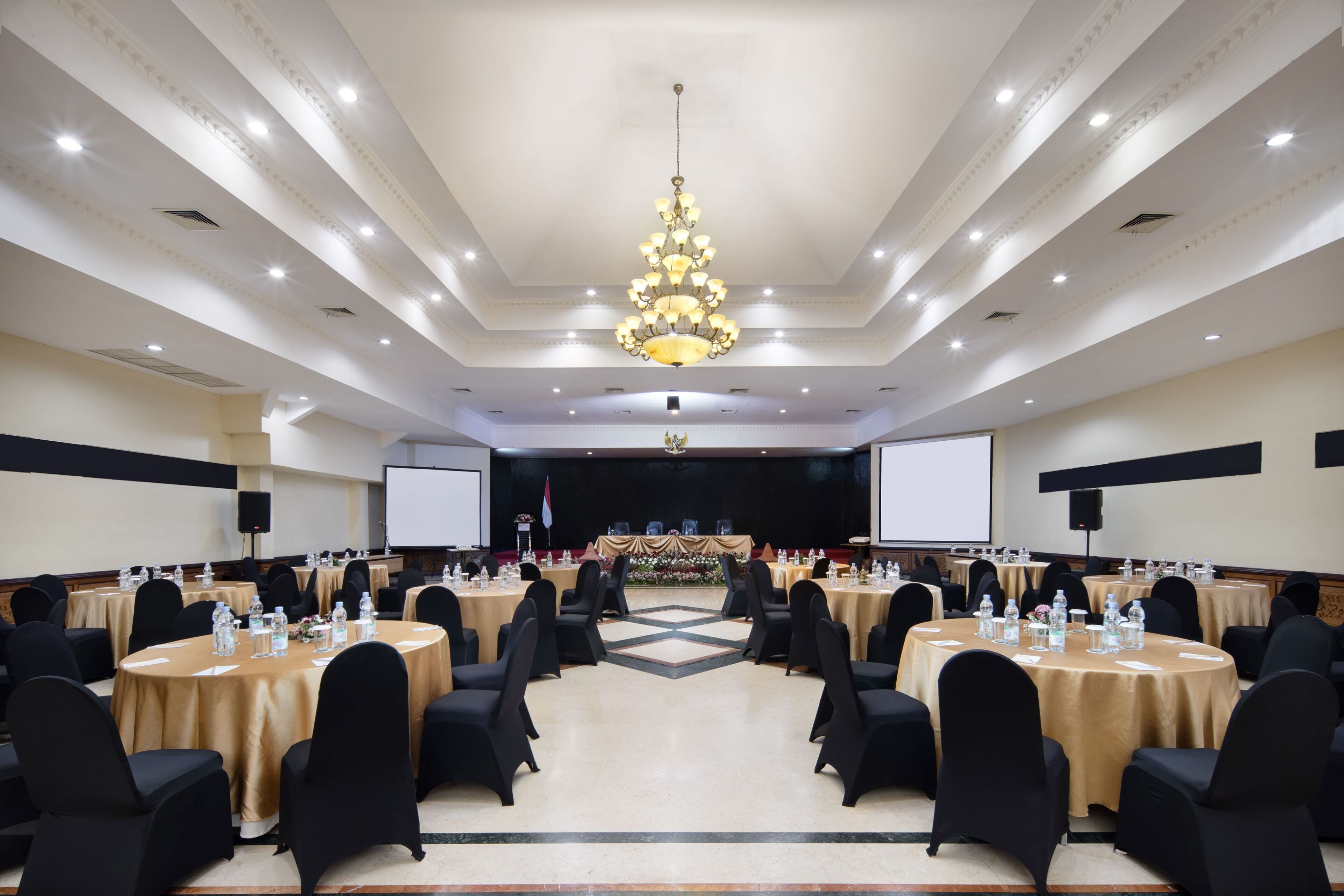 A large conference room with round tables, black chairs, and a central stage.
