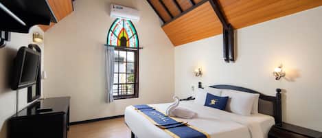 A hotel room with a bed, a television, a desk, and a stained glass window.