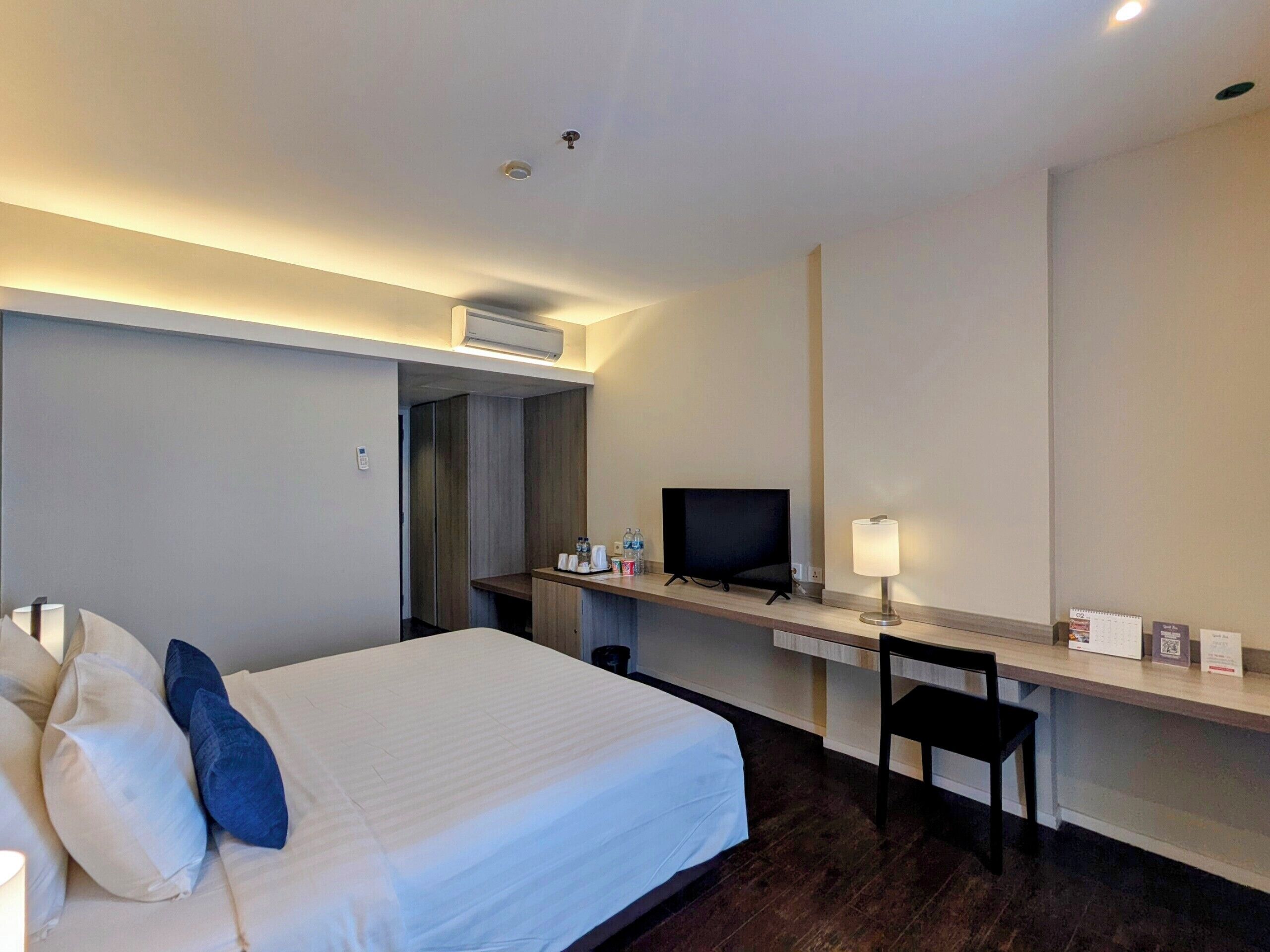 Una habitación de hotel con una cama, un escritorio con una computadora, una silla y un televisor.