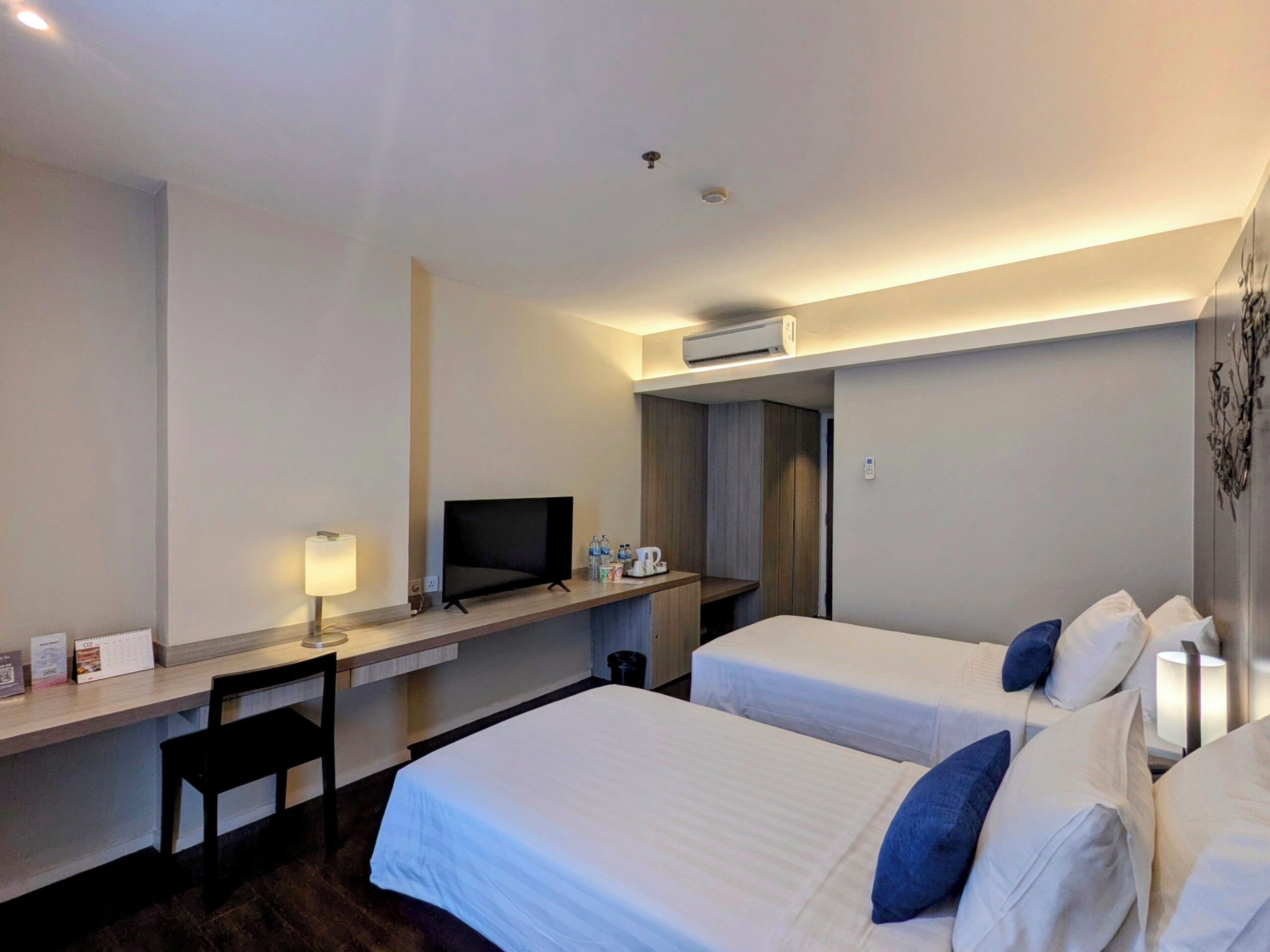 Habitación de hotel con dos camas, un escritorio con computadora, una silla y televisor.