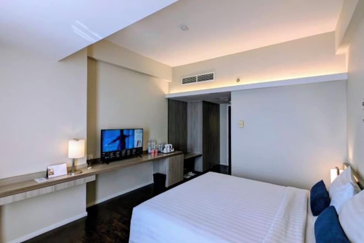 Una habitación de hotel con cama, escritorio, televisor, lámpara y cafetera.