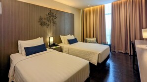 Een hotelkamer met twee bedden, een houten accentmuur, een tafeltje en een raam met gordijnen.