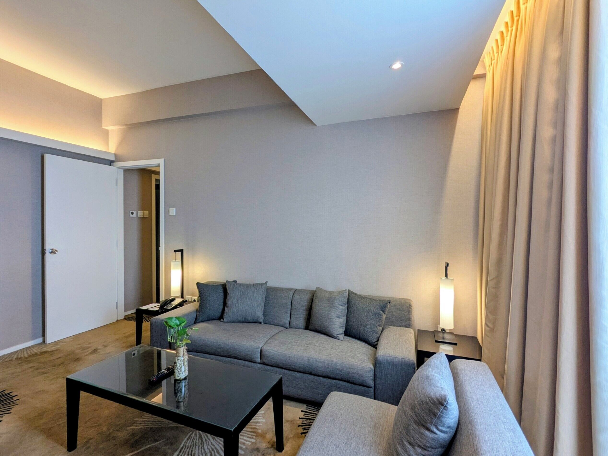 A modern living room with a grey sofa, a glass coffee table, and a lamp.