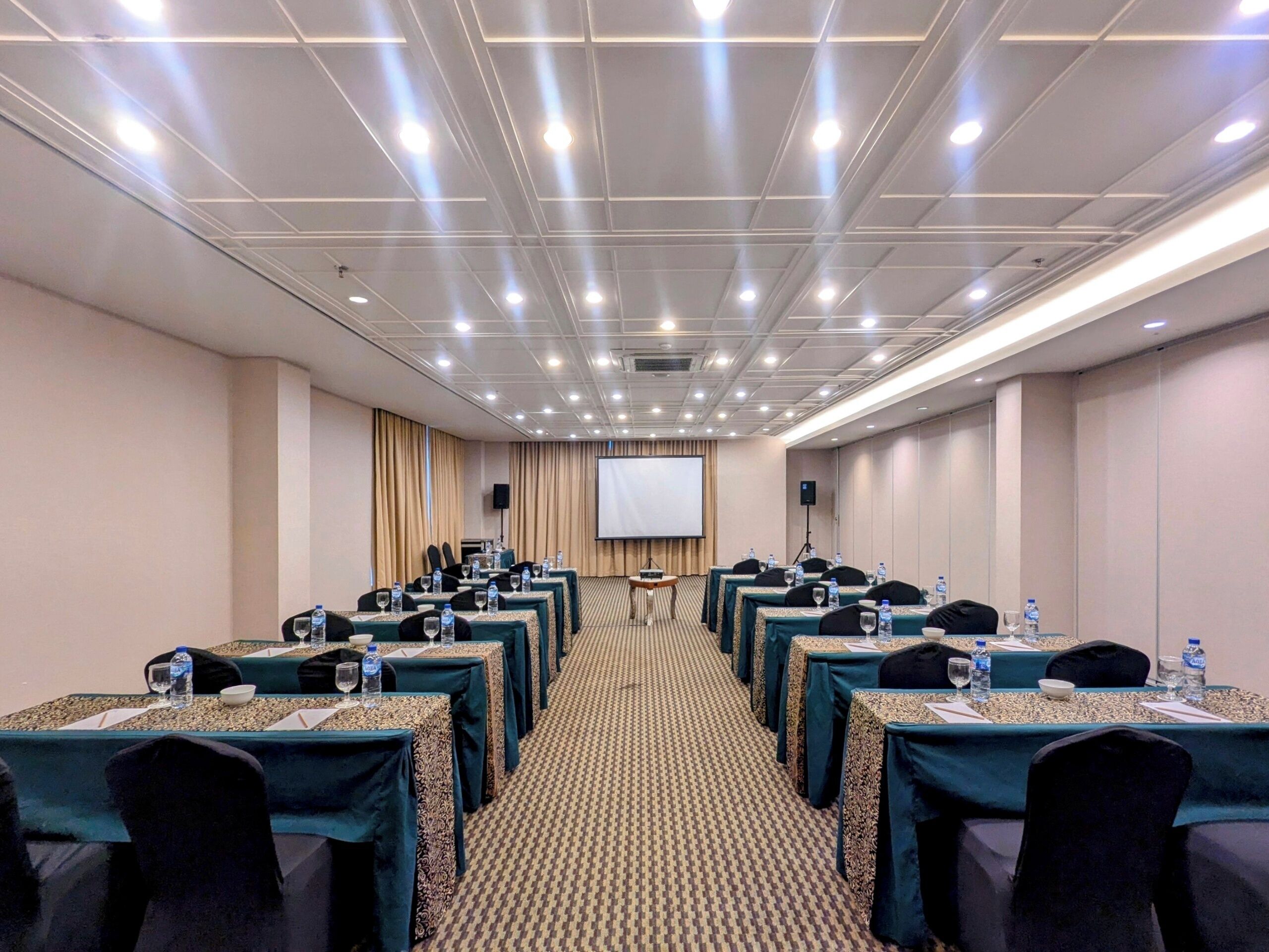 A conference room with rows of tables, chairs, and a projector screen at the front.