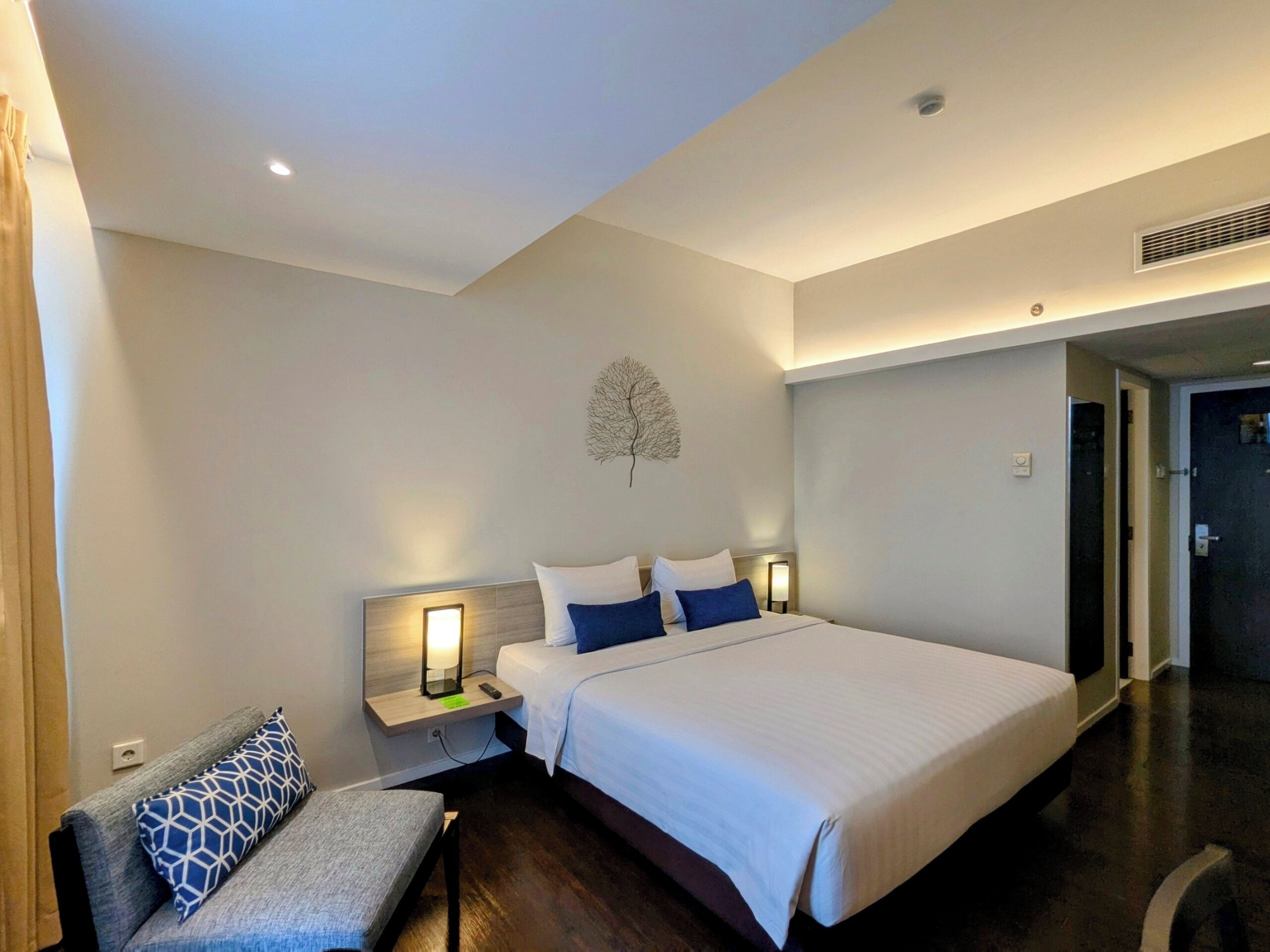 Habitación de hotel con una cama grande, una mesita de noche con lámpara, una silla y una obra de arte en la pared.