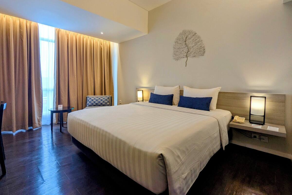 A hotel room with a large bed, two bedside tables with lamps, a chair, and a window with curtains.