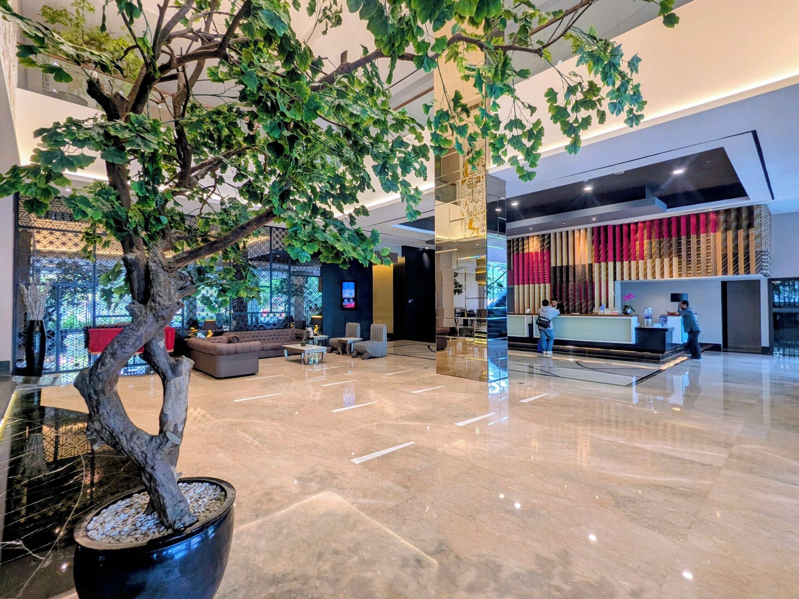 A modern lobby with a large artificial tree, plush seating, a reception desk, and a decorative wall.