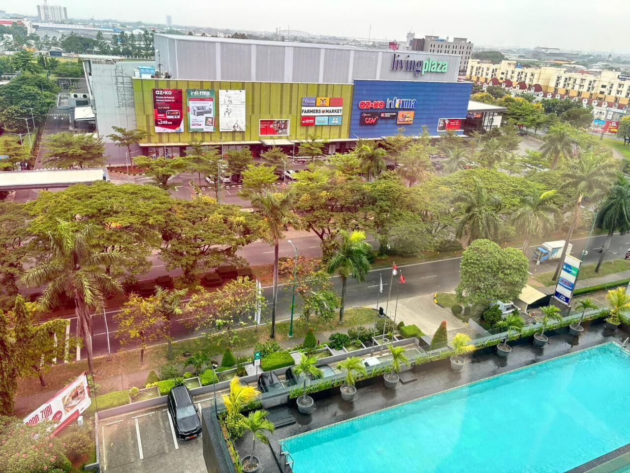 A hotel with a swimming pool, surrounded by greenery and a parking area.