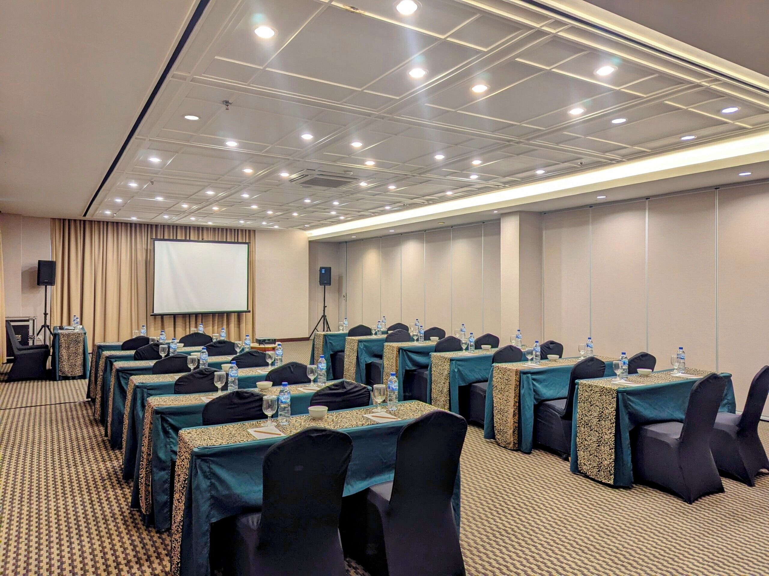 Un salón de conferencias con varias mesas, sillas y una pantalla de proyector.