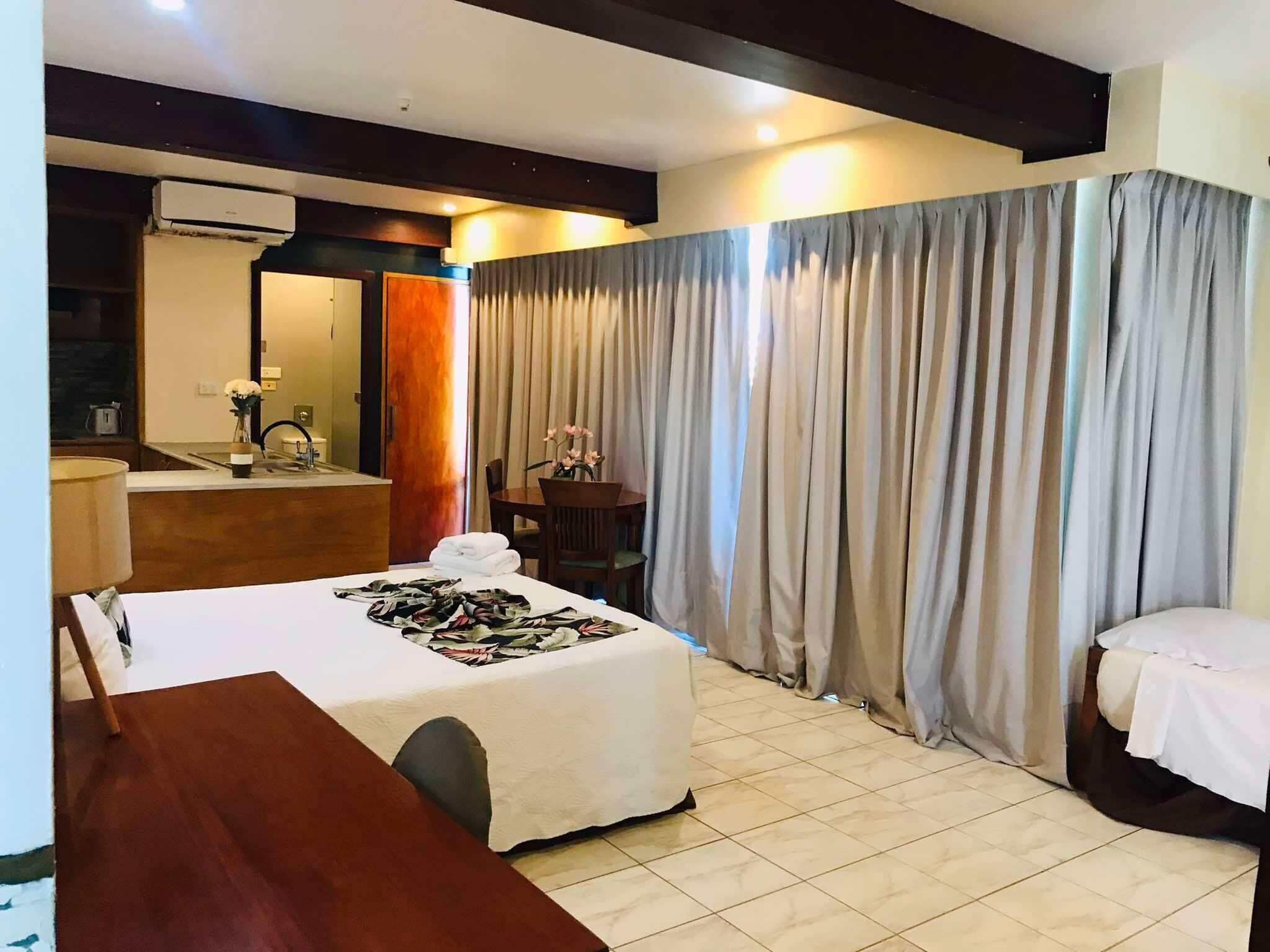 Una habitación de hotel con cama, escritorio, silla, espejo, baño y cortinas.