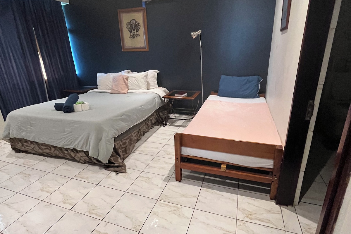 A hotel room with two beds, a bedside table, a floor lamp, and a wall-mounted air conditioner.