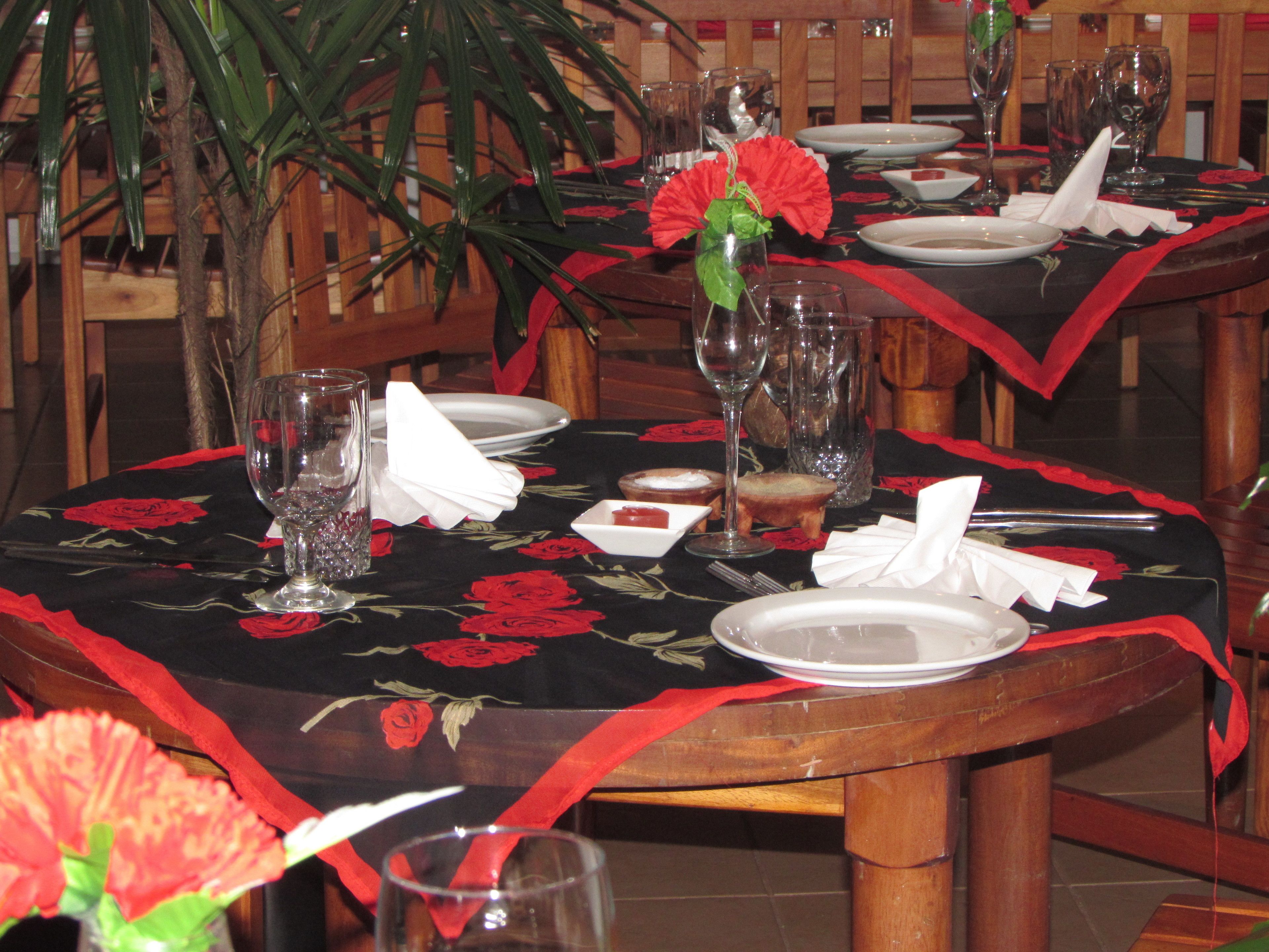 Uma mesa de jantar posta com pratos, copos e um vaso com flores vermelhas.