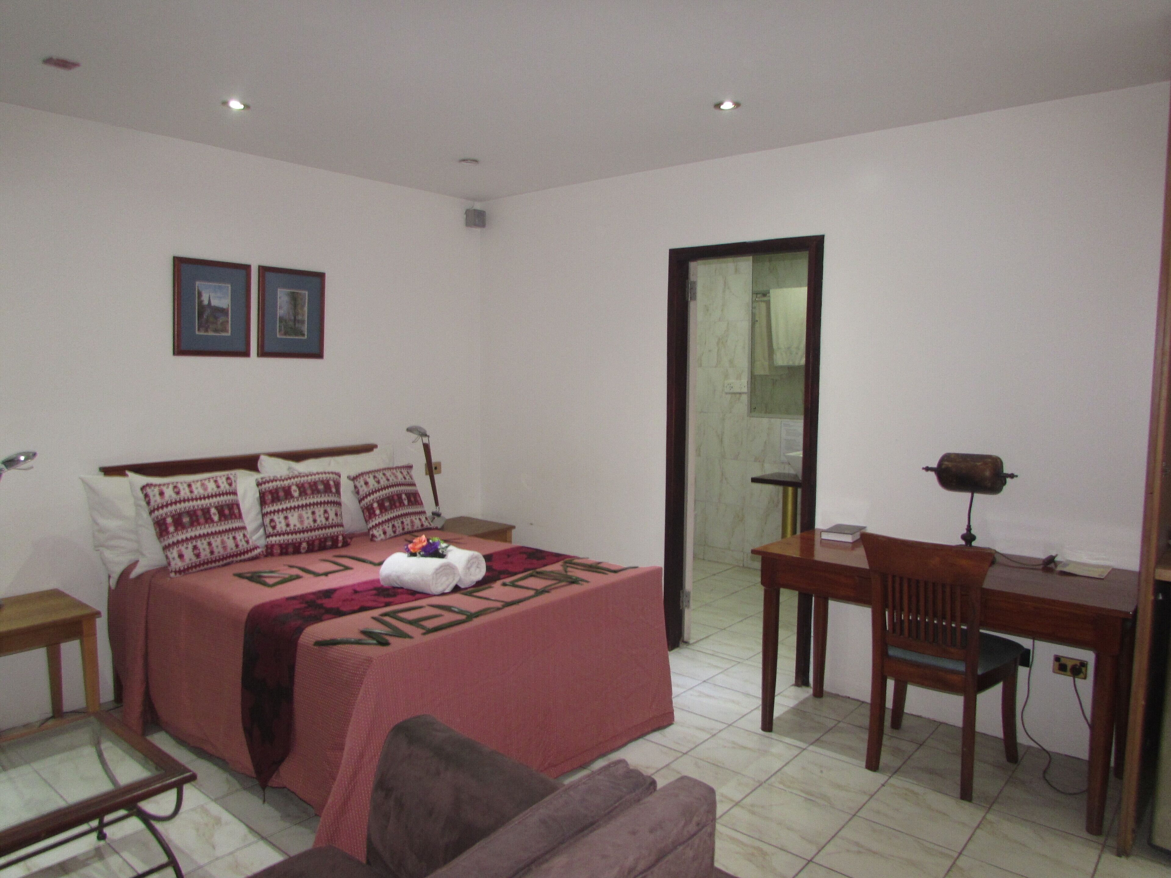 Un dormitorio con una cama, un escritorio, una silla, una mesita y un sofá. Hay una puerta que da al baño.