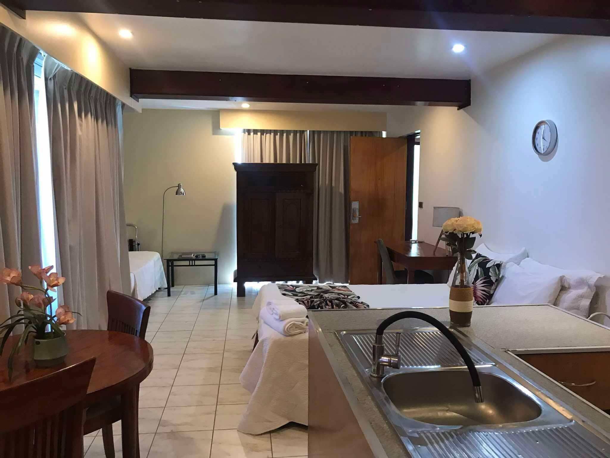 Quarto de hotel moderno com área de jantar, uma cama grande, uma pia e um relógio na parede.