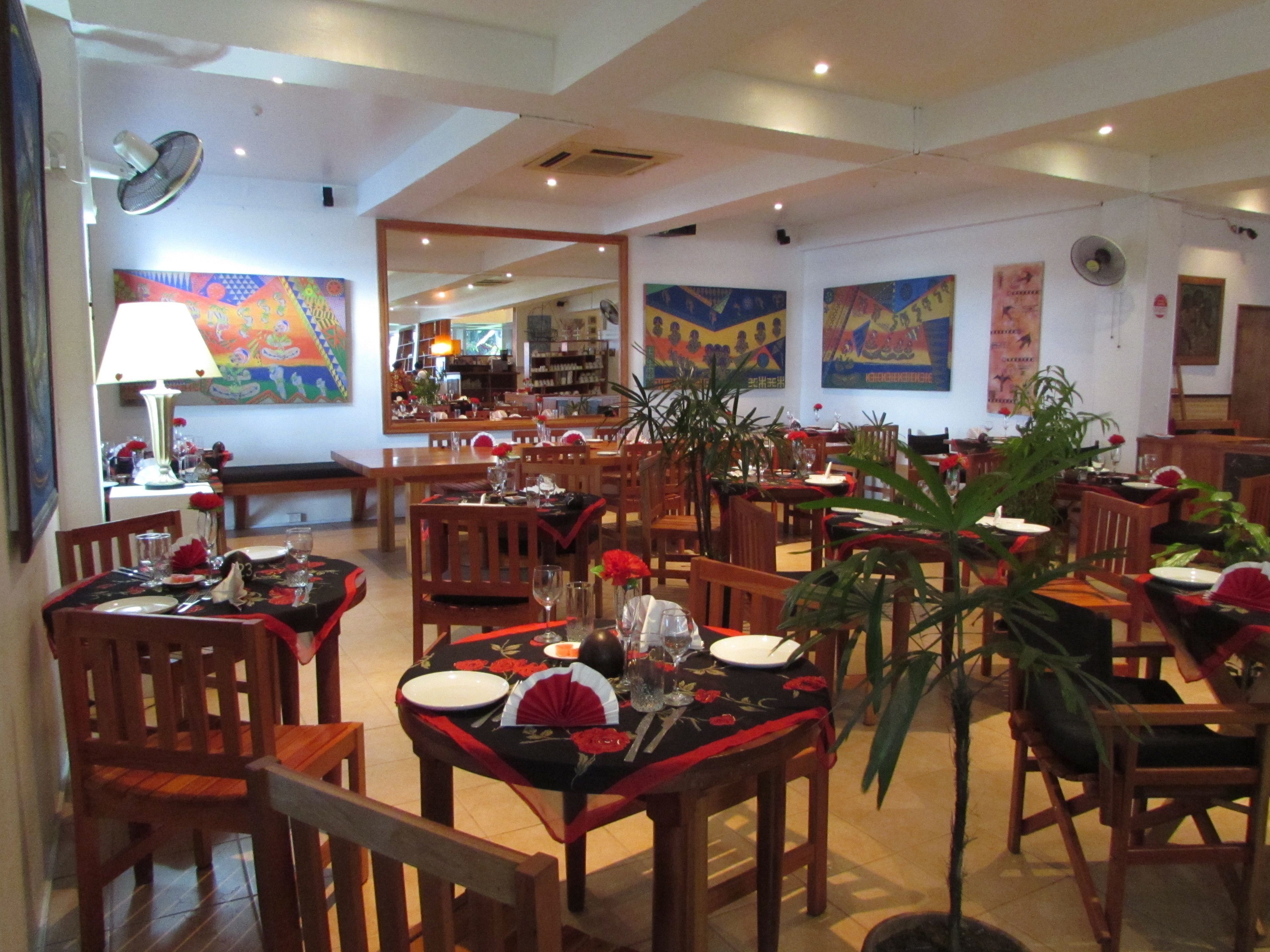 A restaurant with wooden tables and chairs, a mirror reflecting the interior, and colorful wall art.