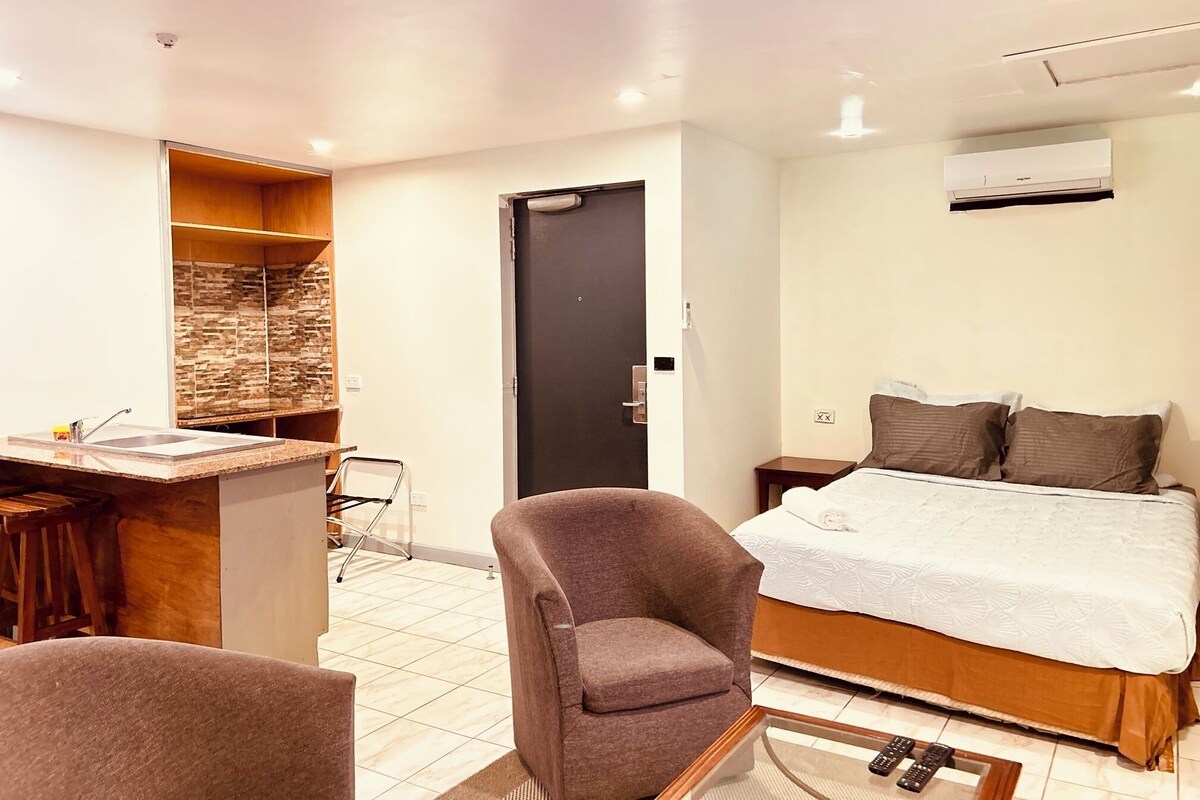 Una habitación de hotel con cama, un escritorio con silla, un armario y un baño con ducha.