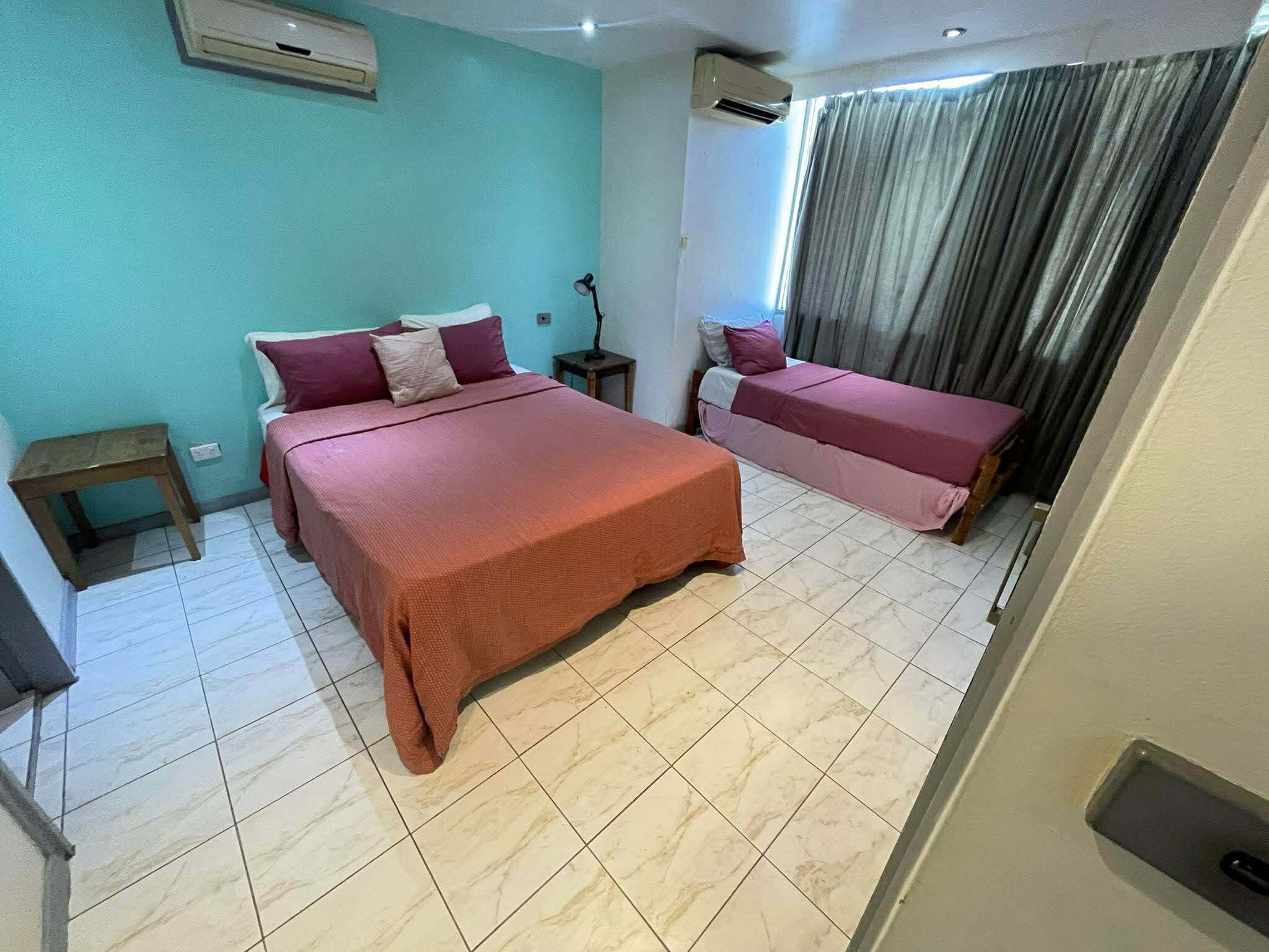 A bedroom with two beds, a nightstand, an air conditioning unit, and a window with curtains.