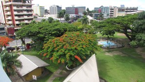 A residential area with a large tree with red flowers, a swimming pool, and a small building. - De Vos on the Park (Suva)