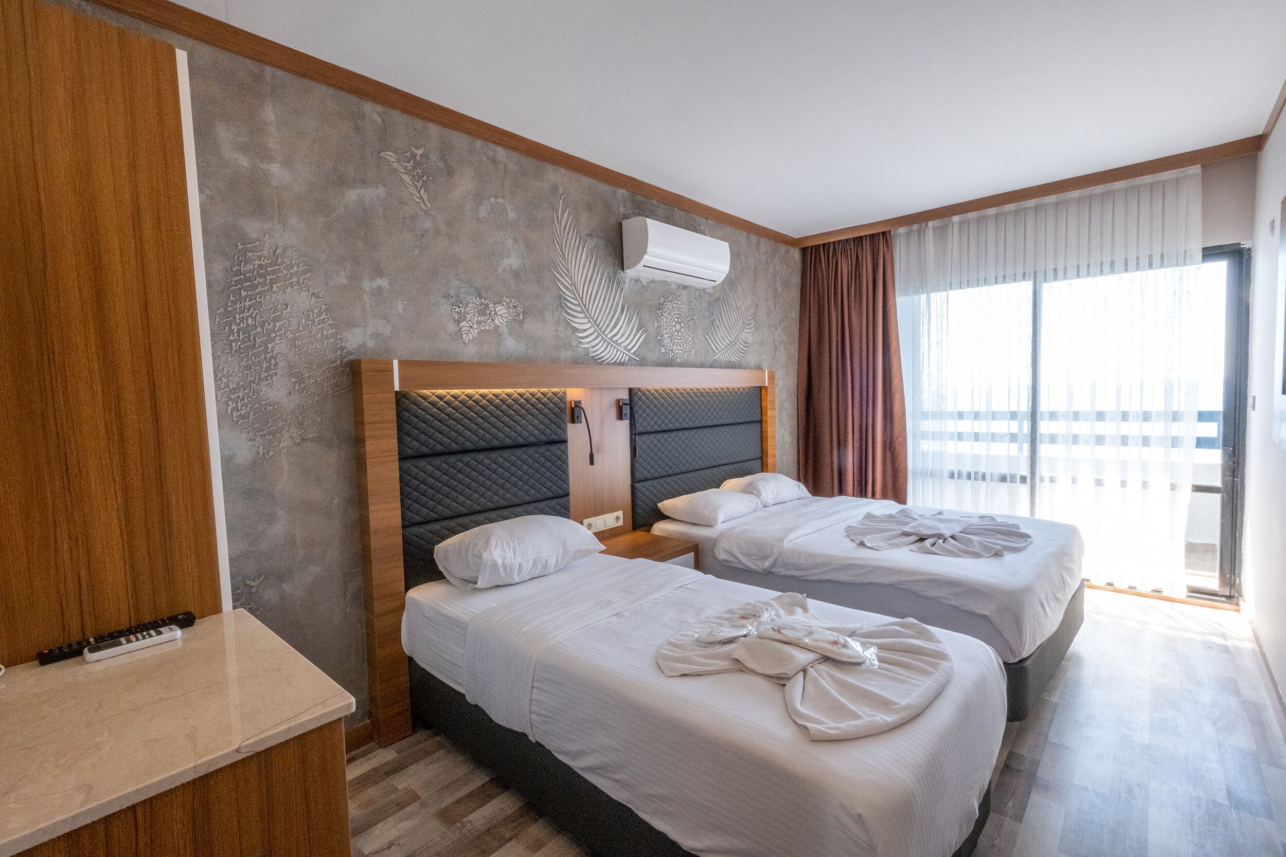 A hotel room with two beds, a wooden panel wall, a large window with curtains, and an air conditioning unit.