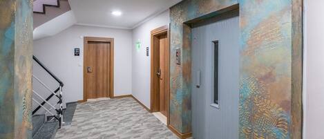 Un pasillo con piso alfombrado, puertas de madera y una escalera con barandilla de metal.