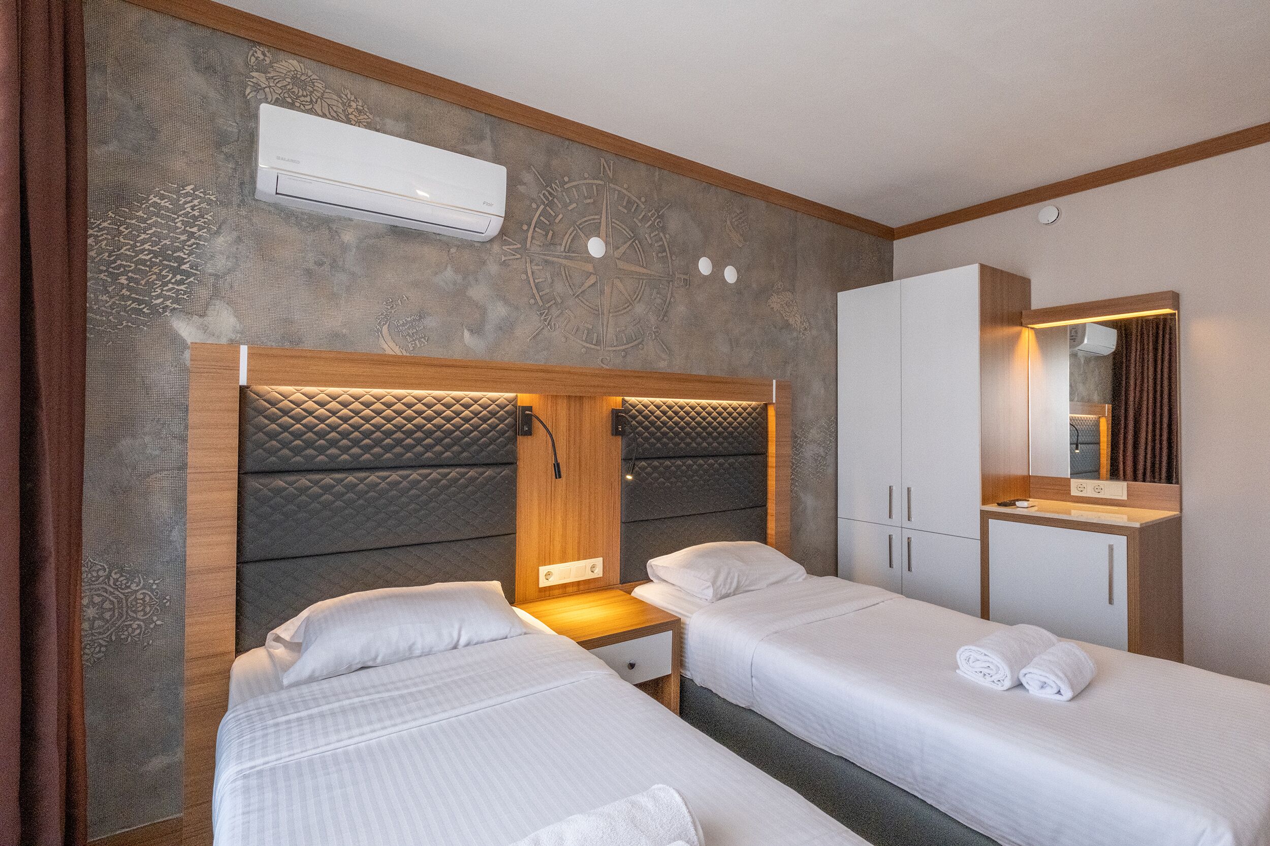A hotel room with two beds, a wooden headboard, a wall-mounted air conditioner, and a mirror above the bed.