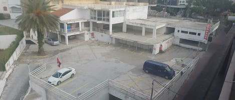 A parking area with a white car and a blue van, surrounded by buildings including a hotel and a multi-story structure.