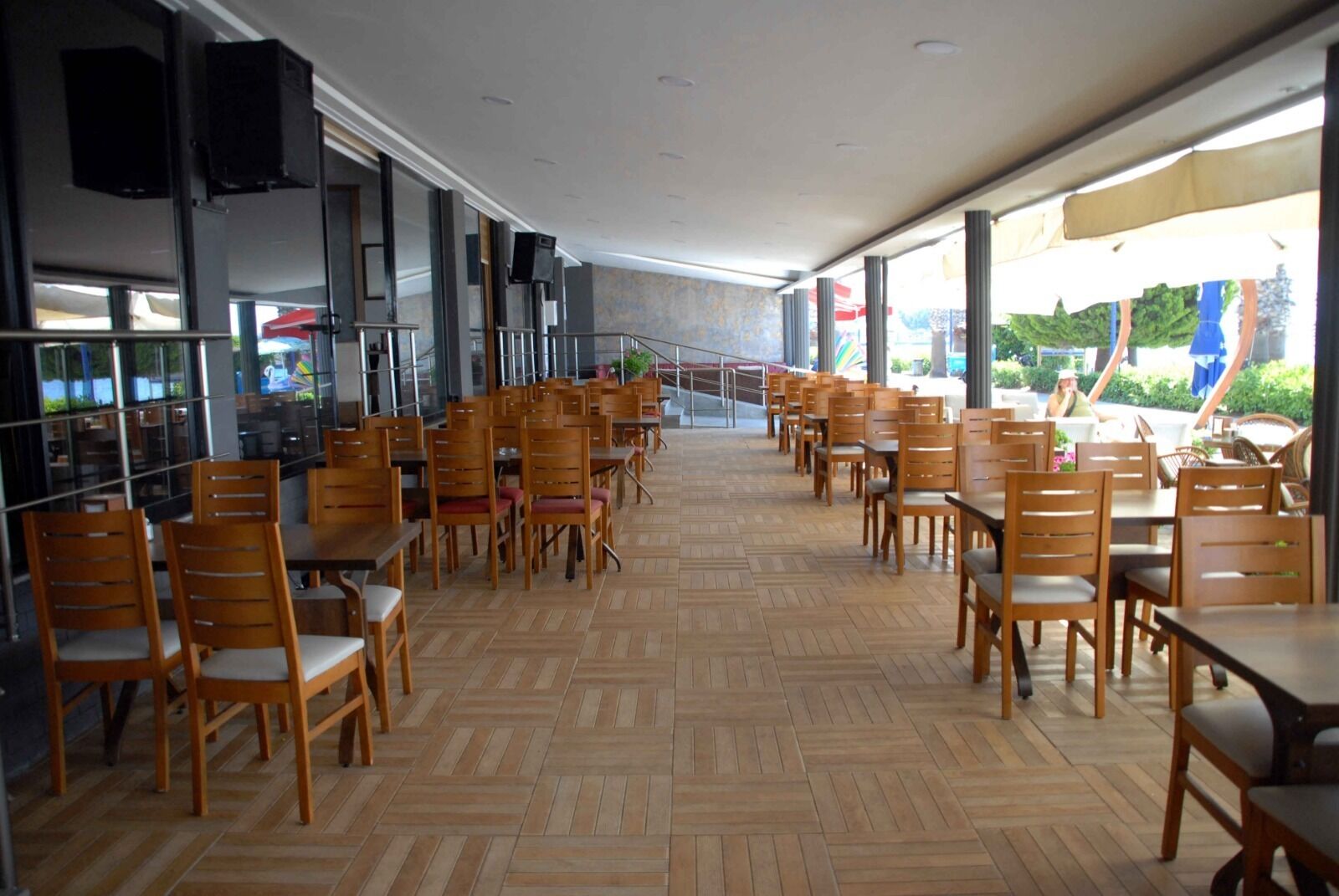 Un vaste espace de restauration intérieur, doté de tables et de chaises en bois, de grandes fenêtres et offrant une vue sur l’extérieur.
