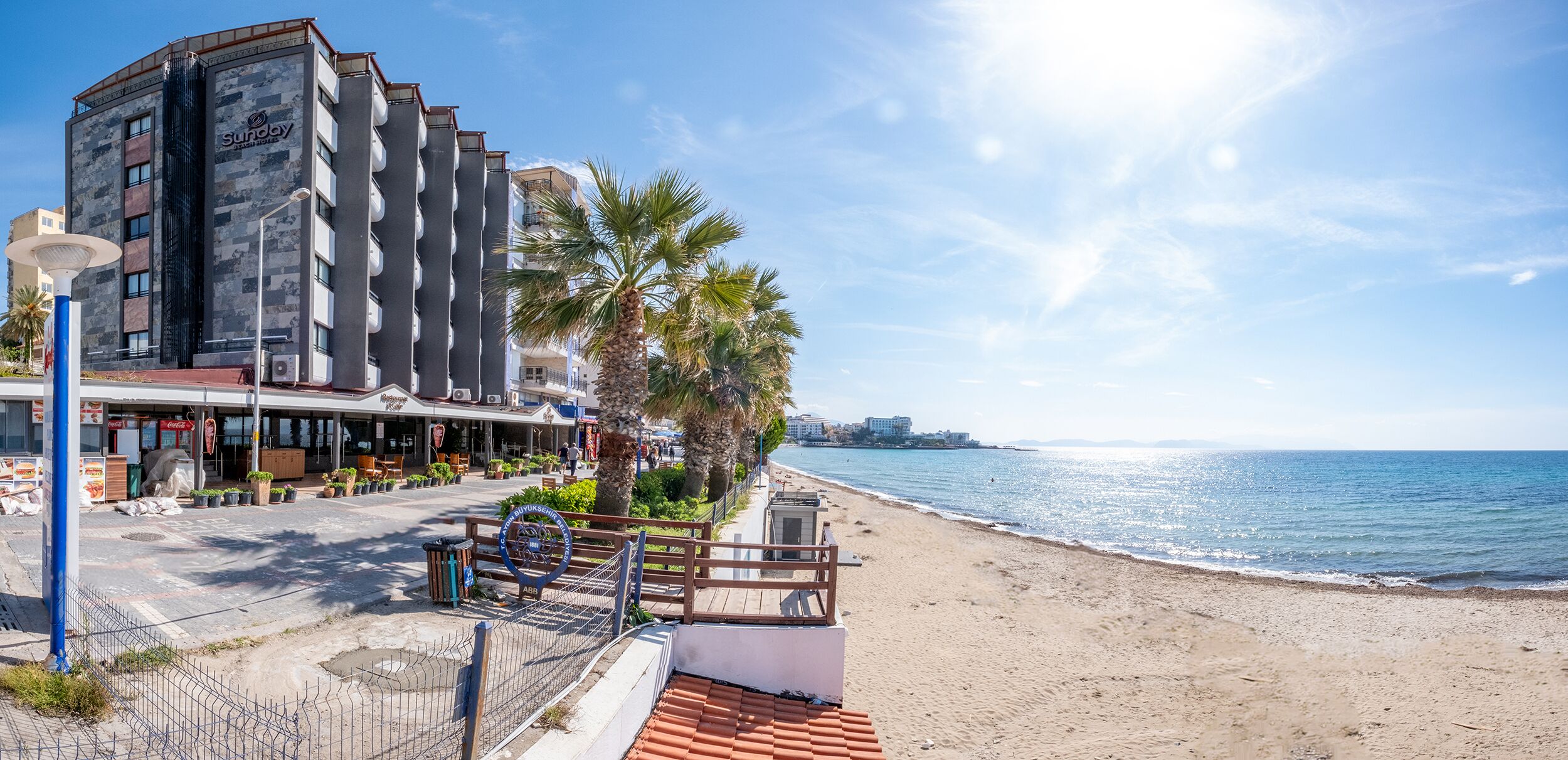 A coastal hotel with a modern design, featuring a prominent 'Sunday' sign, a beachside location, and a view of the sea.